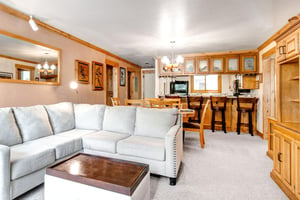 Snow Flower 43s living room looks into the dining area and kitchen and has cream colored carpet and wood trim.