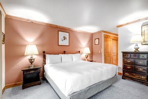 Snow Flower 43s main suite has a king size bed, wooden closet doors, and two night stands and lamps on either side.
