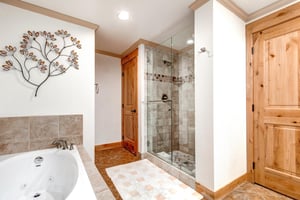 Snow Flower 43s on suite bathroom has a walkin grey tiled shower, deep soaker tub, closet, and white walls with wood trim.