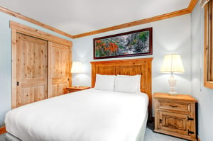 Snow Flower 43s second bedroom has a queensized bed, large wood headboard, white linens, and 2 end tables with lamps.
