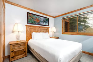 Snow Flower 43s second bedroom has a queensized bed, large wood headboard, white linens, and 2 end tables with lamps.