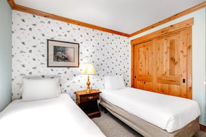 Snow Flower 43s third bedroom has 2 twin beds, one dresser and lamp in the middle, and white wallpaper on an accent wall.