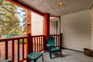 Snow Flower 43s deck with wooden railing, green chair and table, and evergreen trees and blue sky beyond.