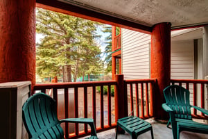 Snow Flower 43s deck with wooden railing, 2 green chairs and table, and evergreen trees and blue sky beyond.