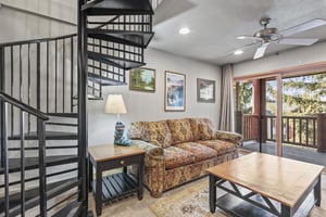 Snow Flower 72s living room with a cozy upholstered couch, coffee table, and black spiral staircase.