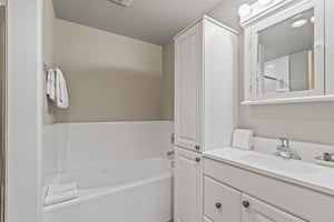 Snow Flower 72s bathroom with greige walls, white cabinetry, bathtub, mirror and vanity light.