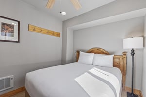 Snow Flower 72s bedroom with a queen bed, white sheets and pillows, greige walls and blonde wood accents.
