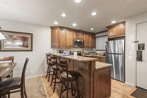 Snow Flower 135s kitchen with medium colored wood cabinets, granite counters, and 3 bar height stools at a breakfast bar.