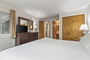 Snow Flower 135s bedroom with king bed, solid wood frame, white linens and wood dresser with TV sitting on it.