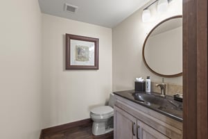 The half bathroom has dark wood floors, grey wood cabinet and single sink vanity.
