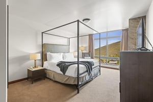 The main suite has a king size bed and is next to floor to ceiling windows that have floor to ceiling drapes.