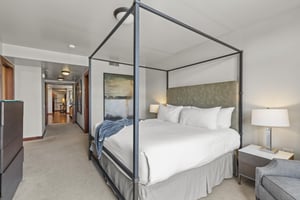 The main suite has a king size bed with a beautiful black iron frame, white linens, and modern art on the wall.