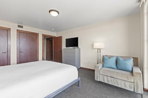 The third bedroom has a king size bed, grey dresser with TV on top, and a oversized comfy chair.