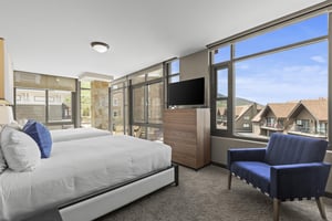 The second bedroom has two queen beds and a wall of window, flat screen TV and blue chair.