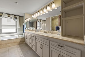 The second bedrooms en suite bathroom has a large two sink vanity, mirror, and lighting.