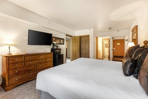 The main suite bedroom has a king size bed, white linens, wooden dresser and flat screen TV.