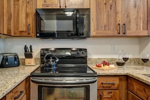 The kitchen has a stainless steel oven, black microwave and wooden cabinets.