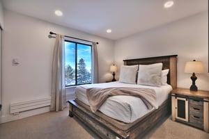 Main bedroom with queen bed and wooden bedframe with large picture window