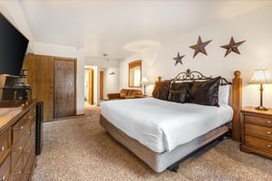 The main suite bedroom has a king size bed, white linens, wooden closet doors and love seat.