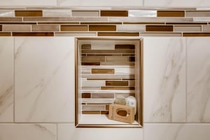 The shared bathroom has gorgeous white tile, with gold and brown decorative tile lining a shelf in the bathtub surround.