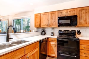 Snow Flower 150s well equipped kitchen with wood cabinets and black appliances.