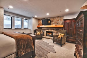 A spacious bedroom with a king size bed and sitting area next to a roaring fire.