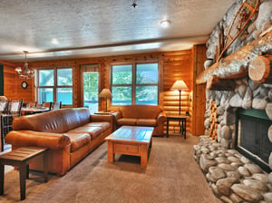 A cozy living room with two leather sofas and a river stone fireplace wall with log mantlepiece.