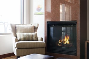 Cozy living room fireplace in granite surround with cream colored accent side chair
