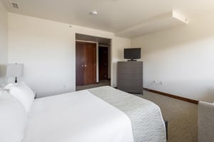 Guest queen bedroom with tall wooden dresser and flat screen TV