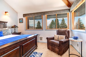 The main suite offers a kingsize bed and large windows framing the evergreen trees.