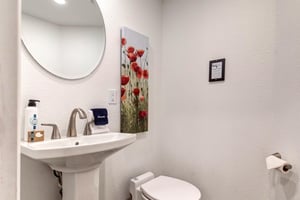 The half bathroom offers a pedestal sink and round mirror.