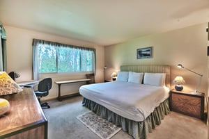Main bedroom with luxurious king bed with white linens and duvet, work desk, and windows overlooking aspen groves