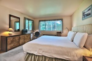 Main bedroom with wooden dresser, TV, and work desk in the corner under the picture window