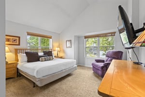 The bedroom has a king size bed and purple sitting chair in the corner.
