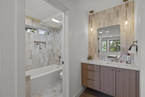 The shared bathroom has been remodeled with wood cabinets and tilework.