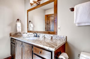 The guest bathroom has a one sink vanity with granite counter and wood cabinet, and large mirror.