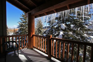 Snow Flower 31s deck with wooden railing, the roof is lined with icecycles, and evergreen trees and blue sky beyond.