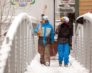 Two skiers walking their skis across the skier access bridge from their skiinskiout property.