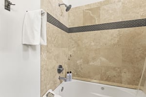 The shared bathroom has a white bathtub and cream tile surround with grey inlayed tile.