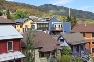 The outside of Town Lift Chalet with a few homes behind it and mountains and forest beyond that.