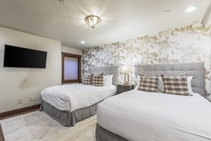 Two queen beds in the lower level bedroom with hardwood floors and large area rug