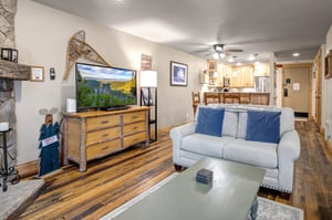 The flat screen TV and comfortable love seat in a cream color.