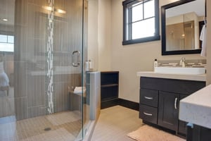 En suite bathroom with walk in grey tiled shower with glass surround
