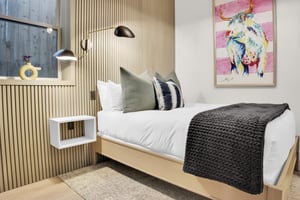 Bedroom with modern wood wall paneling, wall mounted light above free hanging night stand, and queen bed.
