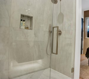 Walk in shower with light grey tile walls and floor and glass shower doors.