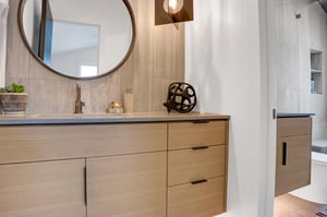 Ensuite guest bathroom with light wood vanity, grey counter, round mirror and artistic lighting.