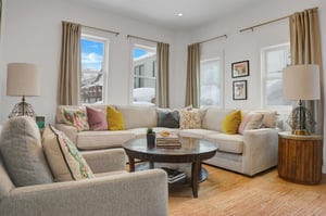 Enjoy the apres room with cream color sectional couch, colorful pillows, white walls, wooden coffee table.