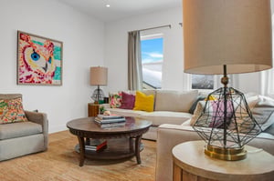 Colorful wall art, stylish end tables and lamps, wooden coffee table, colorful pillows and cream couch in the apres room.
