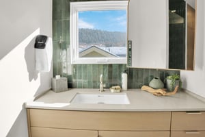 The bathroom has a wood vanity with deep green tile backsplash, window overlooking the mountain and town and large mirror.