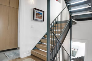 Open staircase for this 4 story home has light wooden treads and black iron railings and frame.